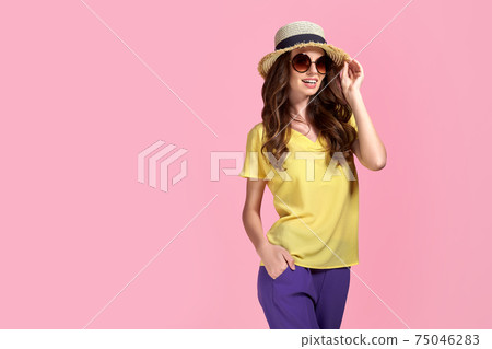 Young girl in sunglasses wearing, colorful clothes and straw hat, isolated over pink background Young girl in sunglasses wearing, colorful clothes and straw hat, isolated over pink background 75046283