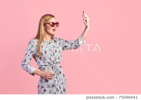 Young girl in sunglasses wearing floral dress, straw hat, isolated over pink background Young girl in sunglasses wearing floral dress, straw hat, isolated over pink background 75046441