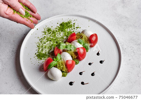 Woman's hands sprinkled with green breadcrumbs to delicious italian caprese salad 75046677
