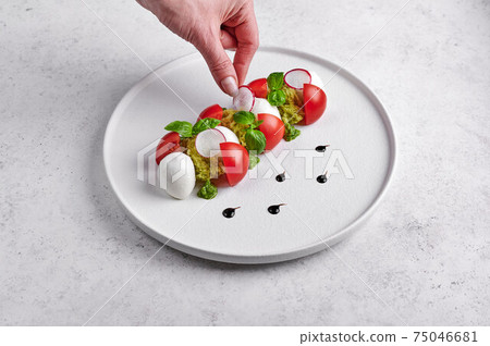 Woman's hand puts the slice of radish to delicious italian caprese salad 75046681