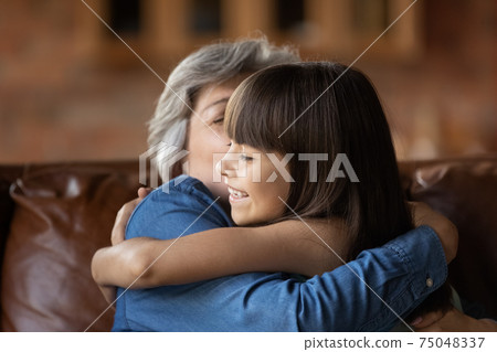 Happy small girl hug mature grandmother at home Happy small girl hug mature grandmother at home 75048337