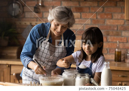 Happy senior grandmother and small granddaughter bake at home Happy senior grandmother and small granddaughter bake at home 75048425