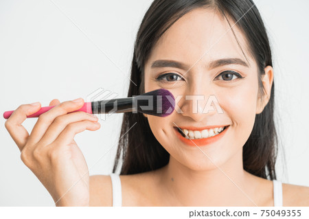 Beautiful young woman applying foundation powder or blush with makeup brush. Mixed race Asian Caucasian model. 75049355