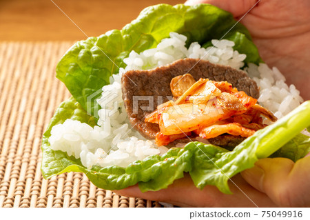 將大米和烤肉包在生菜中，然後食用。 75049916