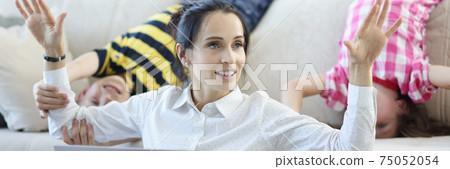 Woman is sitting on floor with laptop raising her hands up behind her children are indulging 75052054