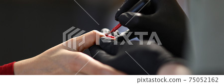 Gloved manicure master paints nails with brush in red. Gloved manicure master paints nails with brush in red. 75052162