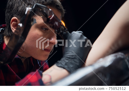 Attractive girl tattoo artist at work, makes a tattoo on the arm of a young woman 75052512
