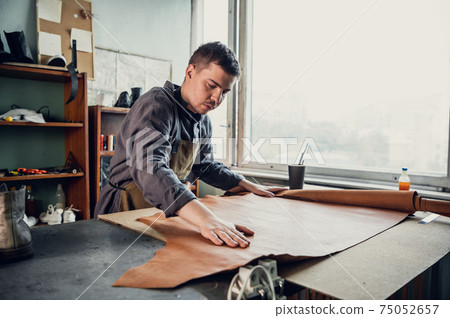 An experienced tanner at his master class shows how to work with leather, lays it out on the table 75052657