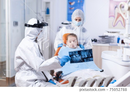Child and mother in ppe suit listening dentist 75052788