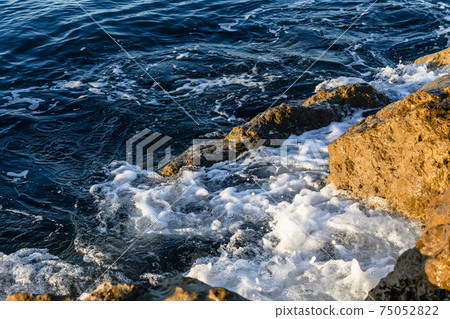 Waves crushing on the rocks on beach in the morning time. Sunrise on the wavy sea with rocks. Waves crushing on the rocks on beach in the morning time. Sunrise on the wavy sea with rocks. 75052822