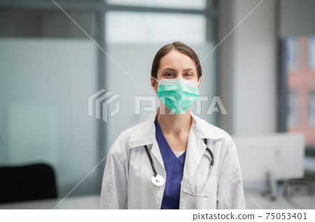 Cute female doctor poses for a photo, looks at the camera in a mask Cute female doctor poses for a photo, looks at the camera in a mask 75053401