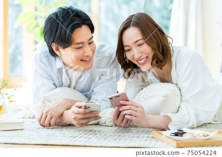 年輕的男人和女人在客廳裡看著智能手機 年輕的男人和女人在客廳裡看著智能手機 75054224