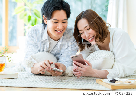 Young men and women looking at smartphones in the living room Young men and women looking at smartphones in the living room 75054225