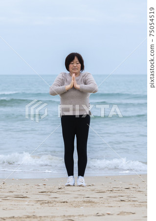 Mature woman practicing meditation near the sea Mature woman practicing meditation near the sea 75054519