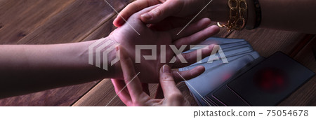 Fortune-teller's hands with prediction cards on a wooden background. The Oracle Visitor draws a card from the divination deck 75054678