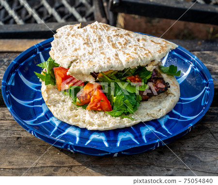 Souvlakia cooked at a campsite fire. Blue plate, red tomatoes, green vegetables, and pita bread 75054840