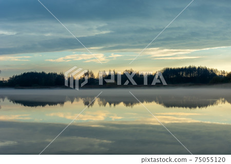 Fog over a calm lake, trees and evening clouds 75055120