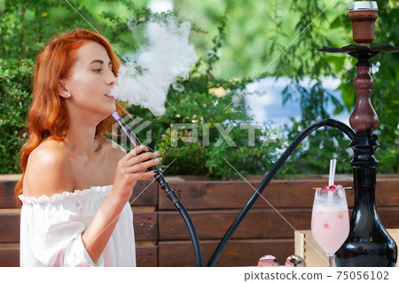 Young women smoke a hookah in a cafe on the street Young women smoke a hookah in a cafe on the street 75056102