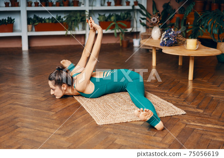 Young slim woman practicing yoga at home doing wide angle seated forward bend pose 75056619
