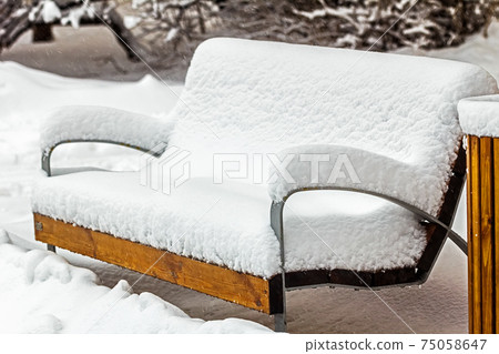 Wooden bench completely covered in snow 75058647