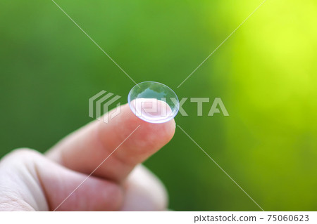 Transparent contact lens on finger tip on blurred green summer nature background 75060623
