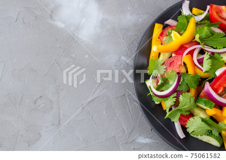 Plate of rainbow salad with different vegetables and herbs on black plate on grey stone background Plate of rainbow salad with different vegetables and herbs on black plate on grey stone background 75061582