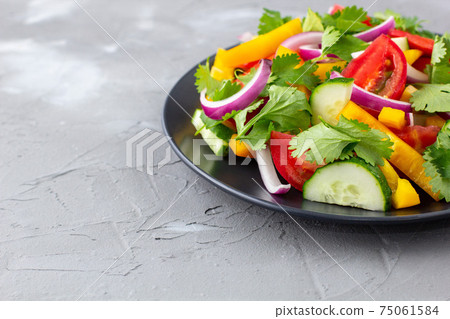 Plate of rainbow salad with different vegetables and herbs on black plate on grey stone background Plate of rainbow salad with different vegetables and herbs on black plate on grey stone background 75061584