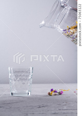 Jug is pouring water into glass cup. 75063122