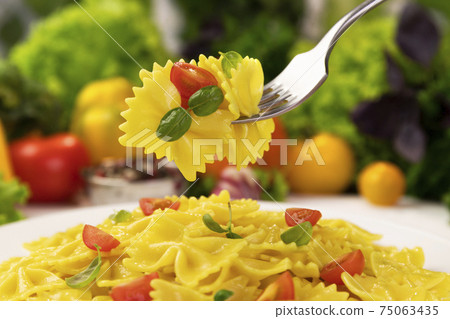 Plate of italian pasta, farfalle on fork with tomatoes and basil Plate of italian pasta, farfalle on fork with tomatoes and basil 75063435