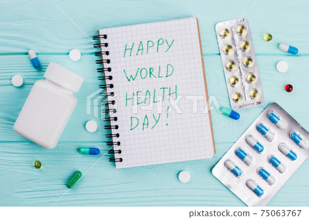 Different pills with notebook and blister packs on blue background. 75063767