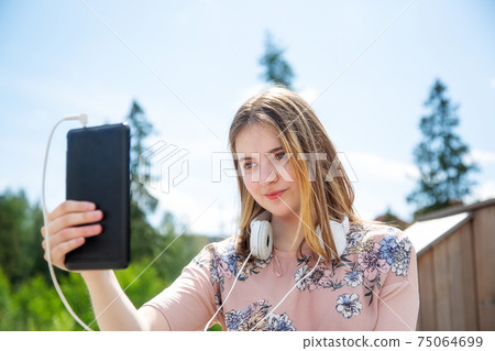 A young girl makes a selfie on her mobile phone while sitting in the park 75064699