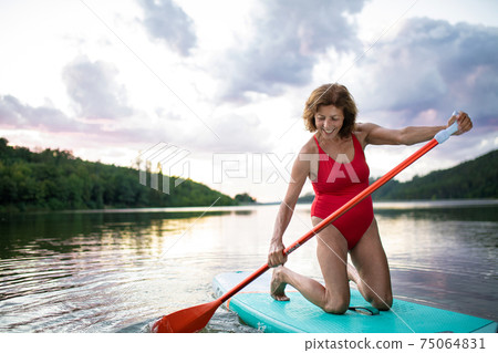 Senior woman paddleboarding on lake in summer. Copy space. Senior woman paddleboarding on lake in summer. Copy space. 75064831