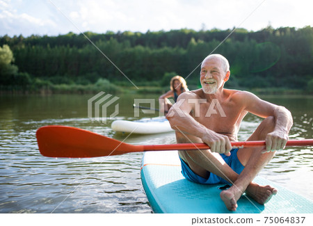 Senior couple paddleboarding on lake in summer. Senior couple paddleboarding on lake in summer. 75064837