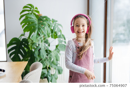 Small girl with headphones indoors at home, looking at camera. 75064907