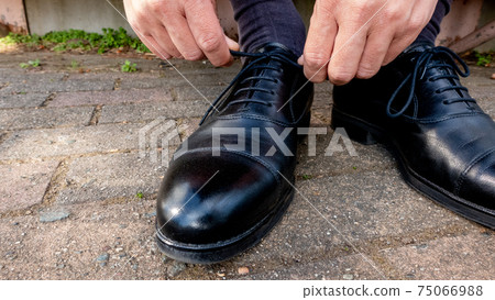 A businessman tying a lace on leather shoes in the park 75066988