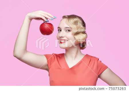 attractive young blonde with a retro hairstyle holds a red apple in her hand 75073263