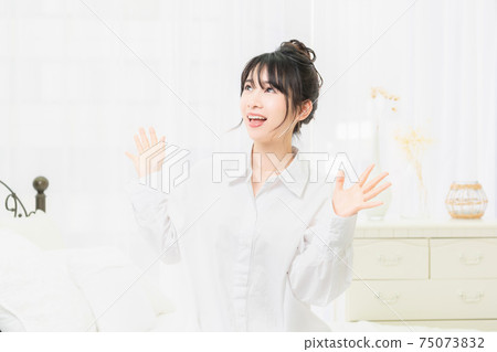 A young woman in a white shirt making a surprise gesture in the room 75073832