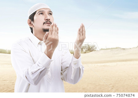 Asian Muslim man standing while raised hands and praying 75074874
