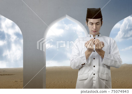Asian Muslim man standing while raised hands and praying 75074943