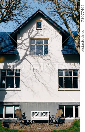 Two folding garden chairs and a white wooden bench, in front of the front of the house in Reykjavik, the capital of Iceland. 75077465