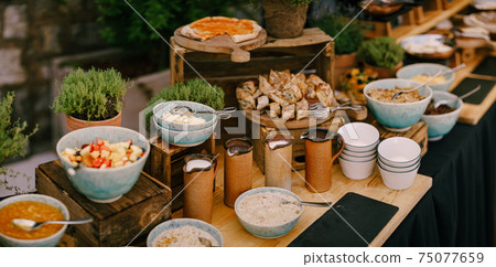 Copper mugs, food plates, and pizza and pastry boards on a long table with kitchen utensils. Buffet table for breakfast in the restaurant. 75077659
