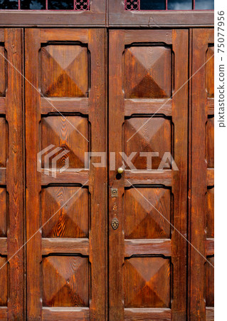 Brown wooden doors with convex squares under a metal grille at the entrance. 75077956