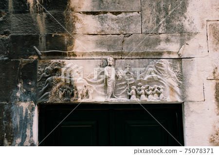 A bas-relief carved in stone on the wall above the black door. 75078371