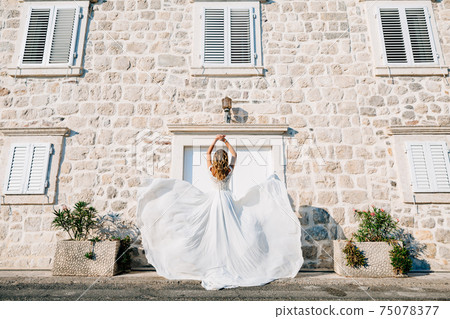 A bride in a wedding dress is spinning on the old street of Perast, her skirt flutters in the wind  75078377