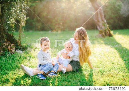 Mother is sitting on the lawn with her two children Mother is sitting on the lawn with her two children 75078391