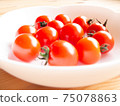 Petit tomatoes on a white plate on a white wooden table 75078863