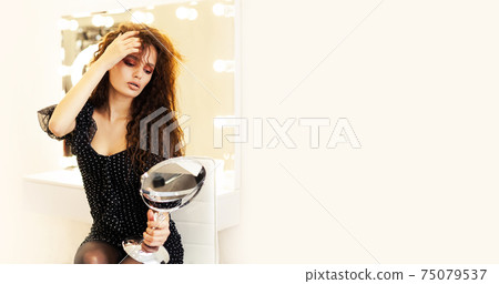 Beautiful girl model brunette, looks in the mirror straightens her hair in a beauty salon. Young 75079537