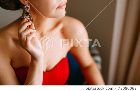 Woman in a red dress is touching her earring Woman in a red dress is touching her earring 75080062
