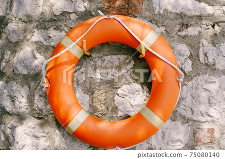 Orange lifebuoy on a gray stone wall. 75080140