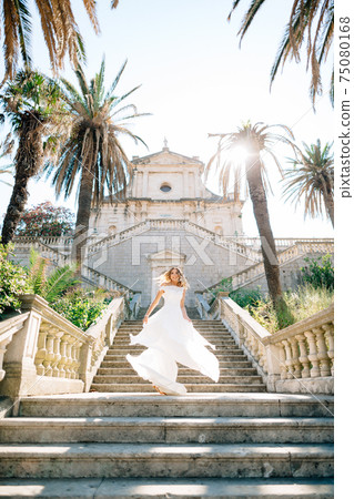 A bride in a wedding dress whirls on the ancient staircase of a temple in Prcanj, her skirt flutters in the wind  75080168